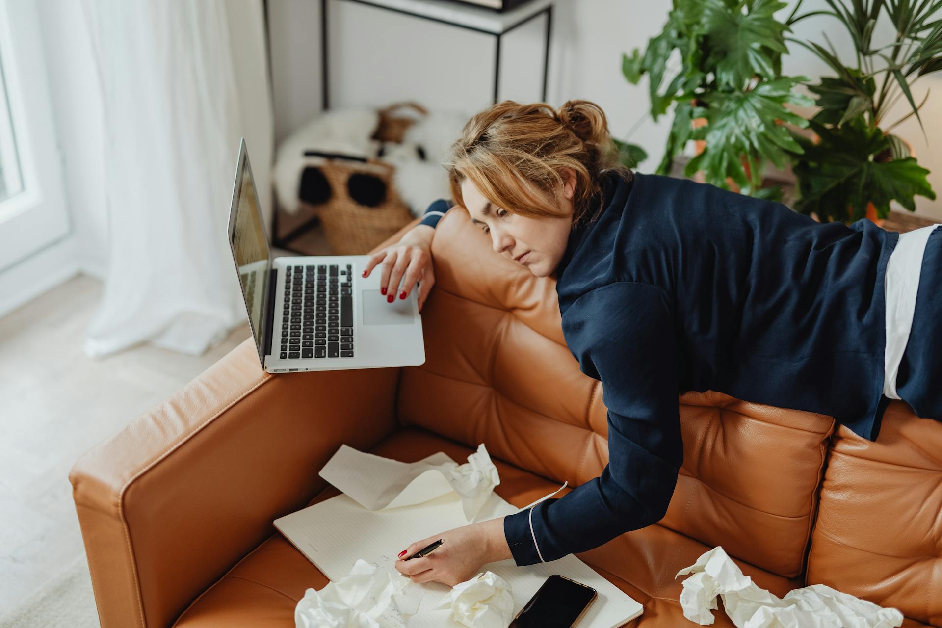 woman lying on couch with laptop and paper